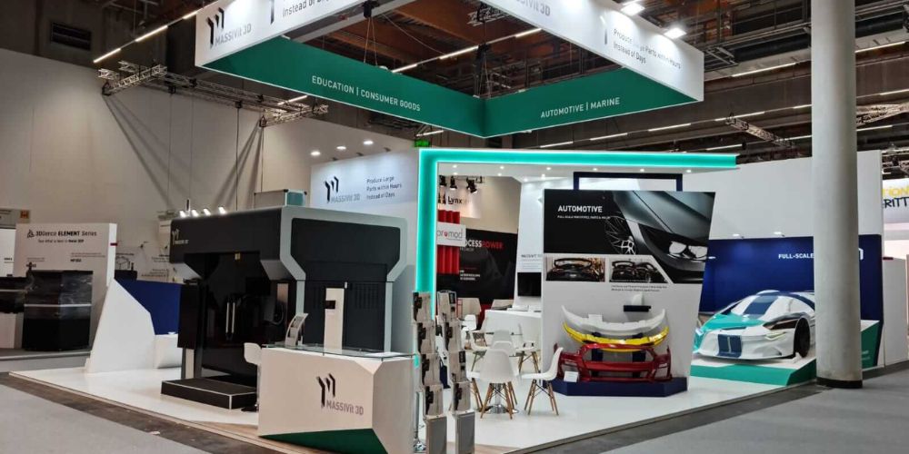 The Massivit booth at the Formnext 2021 features a sleek white and turquoise design complete with a carbon fiber racing car