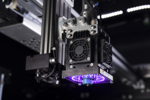 A 3D printing head on a Massivit 3D printing machine with a purple UV curing light 