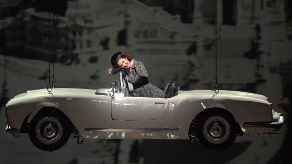 Woman smiling, sitting in 3D printed , suspended vintage car at an opera performance